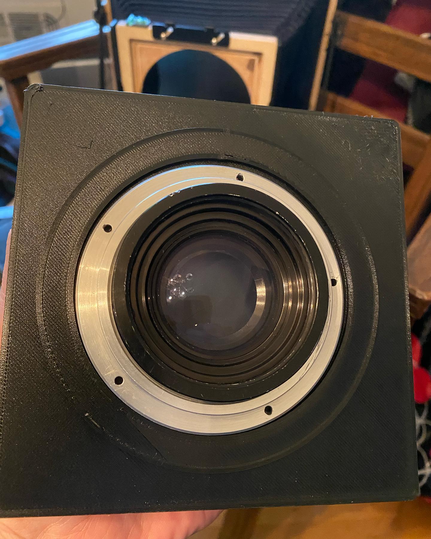 3D printed lens board for my @intrepidcamera 8x10. I had a hard time finding a board that would fit the Ilex No. 4 shutter that came with the Kodak Wide Field Ektar 190mm/f6.3 lens I picked up recently. So I opened up Fusion 360 and made one, which I then printed on my Ender 3 Pro. First attempt didnât work; the hole was based on some specs I read online and was too small, and I hadnât accounted for the rounded corners. Also it wasnât quite thick enough and so wasnât rigid enough. So back to Fusion 360, doubled the thickness to 4mm and added a circle to the back for another 2mm of support. The result looks promising. Will have to take the camera out this week and see if it worked.